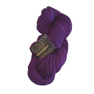 Op de afbeelding: Een streng dieppaars garen met een zwart papieren label met de tekst Cascade Yarns, Distributor of Fine Yarn en Cascade 220. Het garen heeft een getwiste, meeraderige textuur en wordt gepresenteerd in een doorlopende lus voor breiwerk.