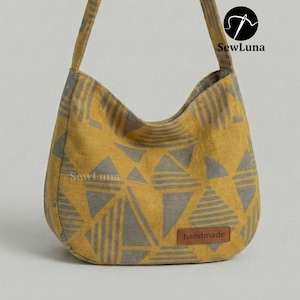 Puede incluir: Bolso de hombro amarillo mostaza con estampado geométrico de triángulos grises. Cuenta con una etiqueta de polipiel marrón que dice "handmade". El bolso tiene una correa larga y está hecho de tela texturizada.