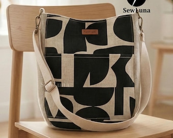 May include: A beige and black patterned shoulder bag with a cream-colored strap and a small "handmade" tag. The bag is sitting on a wooden chair. The bag has a geometric design.
