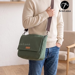 May include: A sage green canvas messenger bag with a fold-over flap, a brown leather-like label reading handmade, and a wide brown adjustable shoulder strap. The bag features the SewLuna logo and text on the flap and in the upper right corner.