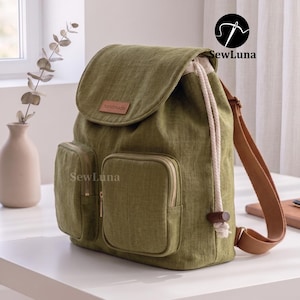 May include: Olive green backpack with two front zippered pockets and a flap closure. Features a drawstring and brown shoulder straps. The word "handmade" is on a small brown tag. The brand name "SewLuna" is visible.