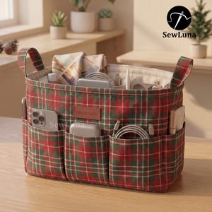 May include: A rectangular fabric storage basket featuring a red and green plaid pattern with two side handles. The front has three exterior pockets containing a smartphone and charging cables. A brown label reads handmade.