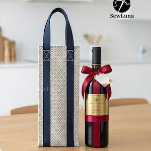 May include: A bottle of wine with a red ribbon and gift tag, beside a patterned wine tote bag with navy blue straps. The wine bottle has a gold label and is on a wooden table.