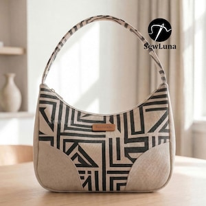 A handmade geometric patterned shoulder bag sitting on a marble table next to a coffee cup and sunglasses. Showcasing the finished result of the Avery shoulder bag PDF sewing pattern with a curved silhouette and top zipper closure.