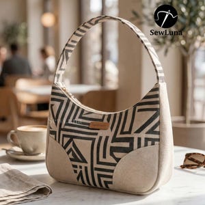 A handmade geometric patterned shoulder bag sitting on a marble table next to a coffee cup and sunglasses. Showcasing the finished result of the Avery shoulder bag PDF sewing pattern with a curved silhouette and top zipper closure.