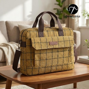 Op de afbeelding: Mosterdgeel en zwart geruite laptoptas met bruine handvatten en een schouderriem. De tas heeft een voorvak met flap en een klein "handmade" label. De tas staat op een houten tafel.