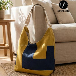 Może przedstawiać: Duża, musztardowo-żółta i granatowa torba typu tote z beżowym paskiem. Torba ma geometryczny wzór bloków kolorów i jest wykonana z miękkiej tkaniny. Torba leży na tkanej macie.