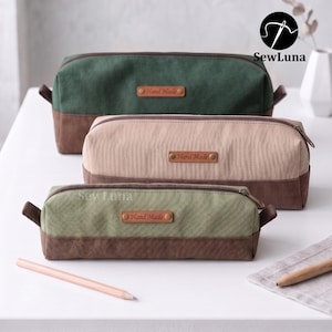 Puede incluir: Tres estuches rectangulares con cremallera de diferentes tamaños, con un diseño bicolor que combina una parte superior lisa y una base más oscura. Cada estuche incluye una etiqueta de cuero sintético marrón con el texto Hand Made.
