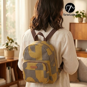 Puede incluir: Una pequeña mochila con un estampado geométrico en amarillo mostaza y gris. La mochila tiene correas marrones y un bolsillo delantero. La palabra "handmade" está en una pequeña etiqueta marrón en el bolsillo delantero. La marca "SewLuna" es visible.