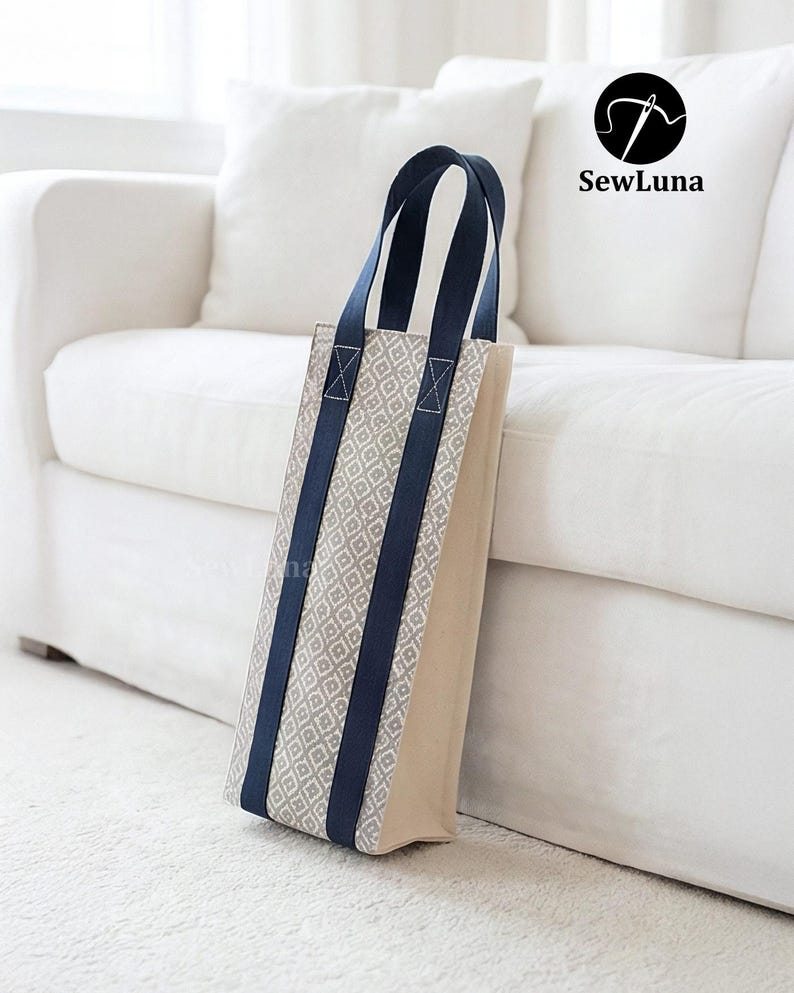 Tall fabric wine bottle carrier with a grey geometric pattern and navy straps, standing on a wooden table next to a wine bottle tied with a red ribbon. Modern kitchen background. Represents a digital sewing pattern for a reusable wine tote bag.