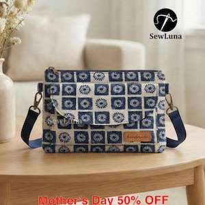 Puede incluir: Bolso bandolera con estampado azul y blanco con cierre de solapa y correa ajustable, sobre una mesa de madera. El bolso presenta un diseño floral repetido y una pequeña etiqueta "handmade". El texto "SewLuna" es visible.