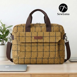 Mustard yellow plaid handmade laptop bag sewing pattern featuring brown webbing handles, an adjustable shoulder strap, a top zipper, and a front flap pocket, displayed on a clean white background.