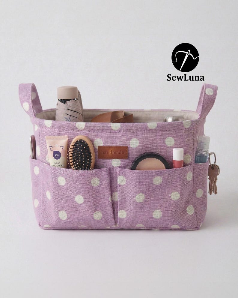 Purple polka dot handmade fabric purse organizer bag filled with daily essentials like a hairbrush, hand cream, and keys. A PDF sewing pattern project for a bag insert or desk storage bin displayed on a clean white background.