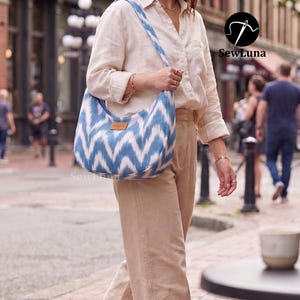 Puede incluir: Un bolso de hombro en forma de media luna con un patrón de chevrón azul y blanco estilo ikat. El bolso tiene una sola correa ancha y una pequeña etiqueta rectangular marrón en la parte delantera. La tela tiene una textura tejida suave.