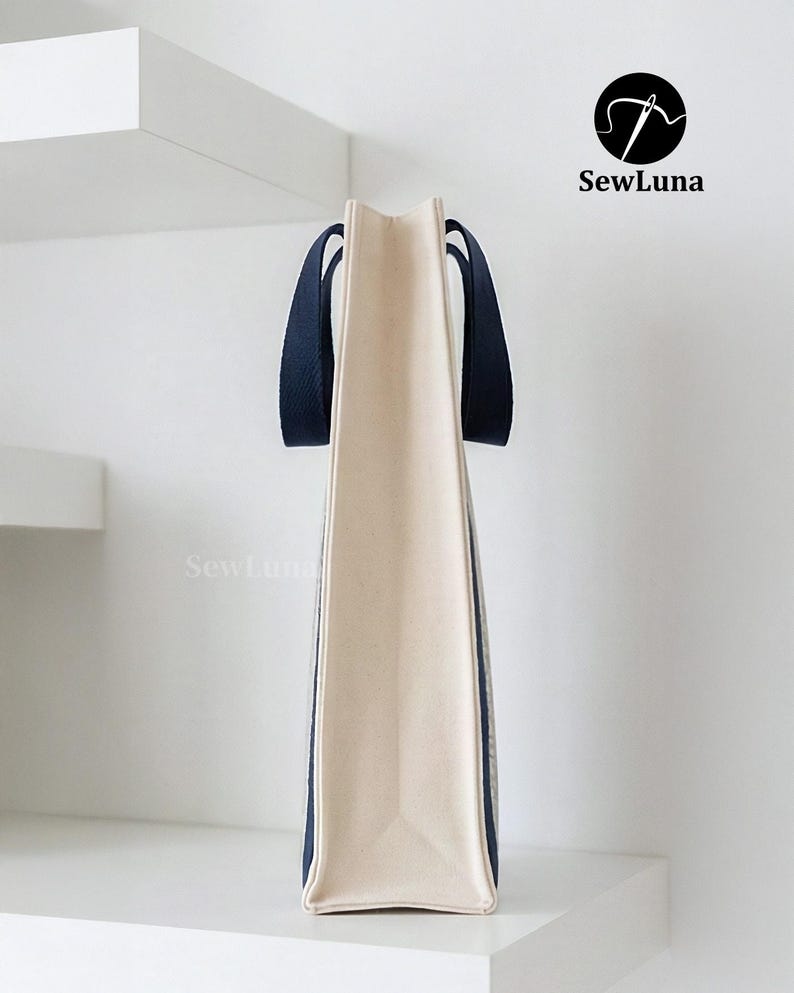 May include: A beige tote bag with navy blue handles and trim. The bag is rectangular with a flat bottom and is displayed against a white background. The SewLuna logo is visible in the upper right corner.