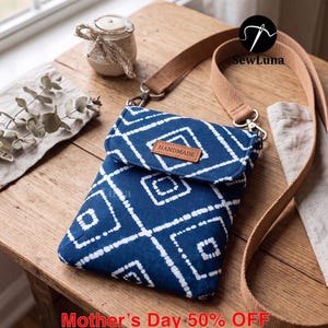 Puede incluir: Un bolso bandolera hecho a mano con estampado azul y blanco y correa marrón. El bolso tiene cierre de solapa y una pequeña etiqueta de cuero que dice "HANDMADE". El texto "Mother's Day 50% OFF" es visible en la parte inferior.