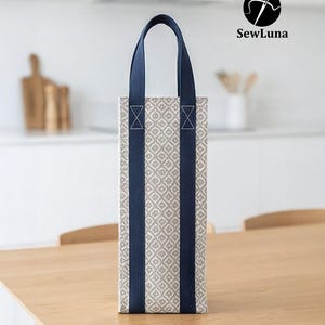 Tall fabric wine bottle carrier with a grey geometric pattern and navy straps, standing on a wooden table next to a wine bottle tied with a red ribbon. Modern kitchen background. Represents a digital sewing pattern for a reusable wine tote bag.