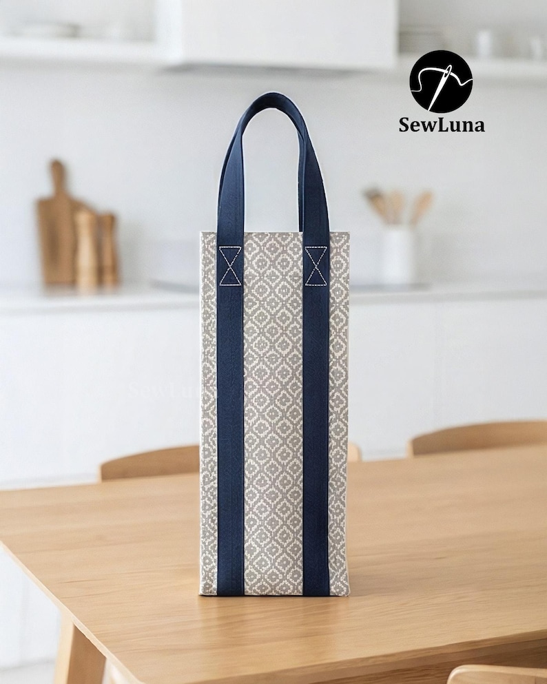 Tall fabric wine bottle carrier with a grey geometric pattern and navy straps, standing on a wooden table next to a wine bottle tied with a red ribbon. Modern kitchen background. Represents a digital sewing pattern for a reusable wine tote bag.