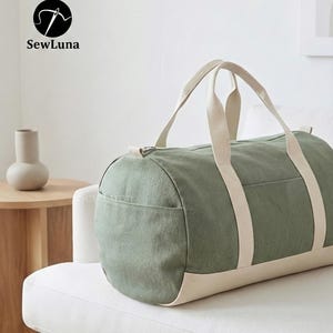 Minimalist earthy green and beige canvas duffle bag sewing pattern PDF with sturdy webbing handles and a side pocket, displayed against a light grey background. Perfect weekender bag sewing project.