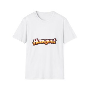 Könnte beinhalten: Weißes T-Shirt mit dem Wort "Huereguet" in einer Retro-Schriftart mit orange-gelbem Farbverlauf und dunkler Umrandung. Das T-Shirt hat kurze Ärmel und einen Rundhalsausschnitt.