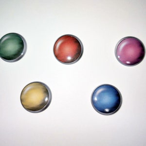 May include: Five round, colorful magnets with metallic silver rims are arranged on a white surface. The magnets are in shades of green, red, pink, yellow, and blue. The colors have a gradient effect, with lighter centers and darker edges.