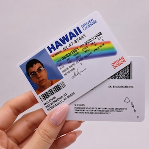 May include: A white plastic Hawaii driving licence card featuring a rainbow graphic, the name McLovin, and a photograph of a person wearing glasses. The card displays text including Hawaii, Driver License, Organ Donor, and address details in Honolulu.