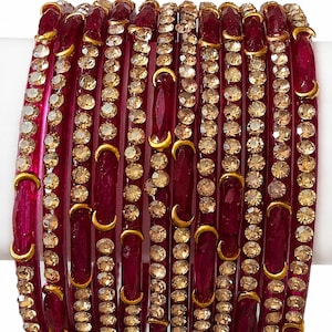 Puede incluir: Un conjunto de pulseras rojas con detalles dorados y pedrería incrustada. Las pulseras están dispuestas verticalmente, mostrando su intrincado diseño y detalles brillantes. Los detalles dorados tienen forma de media luna.