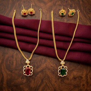 May include: Two gold-tone necklaces with matching stud earrings. One set features a rectangular red gemstone pendant surrounded by small clear stones, and the other set features a rectangular green gemstone pendant with clear stones.