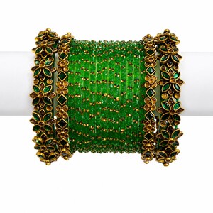 Op de afbeelding: Een set groene glazen armbanden met goudkleurige bloemen en geometrische accenten. De armbanden worden gepresenteerd op een witte ondergrond, waarbij de ingewikkelde details van de sieraden worden benadrukt.