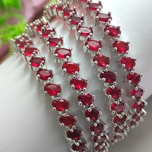 Può includere: Un set di quattro bracciali rigidi color argento, ciascuno caratterizzato da una fila continua di pietre preziose ovali rosso scuro incastonate in montature di metallo. I bracciali sono disposti in parallelo, mostrando il colore rosso.