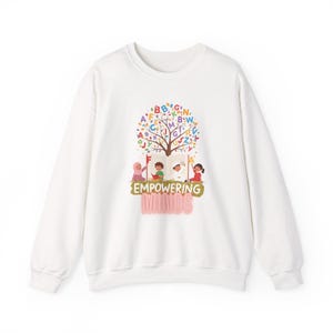 May include: White sweatshirt with a colorful graphic. The graphic features a tree with letters as leaves, an open book, and children. The text "EMPOWERING MINDS" is below the image. A long-sleeved, crew neck sweatshirt.