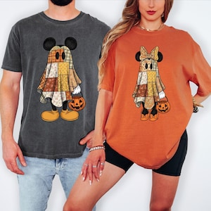Peut inclure: Un t-shirt gris anthracite et un t-shirt orange, chacun arborant un motif de personnage déguisé en fantôme sous un drap en patchwork. Le personnage fantôme sur le t-shirt gris a des oreilles rondes, tandis que celui sur l'orange a un nœud.