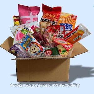 Pode incluir: Uma caixa de cartão cheia de snacks japoneses, com a etiqueta "JAPANESE SNACK BOX". Oferece três tamanhos: Pequeno (15 snacks), Médio (30 snacks) e Grande (50 snacks). Os snacks variam consoante a época e a disponibilidade.