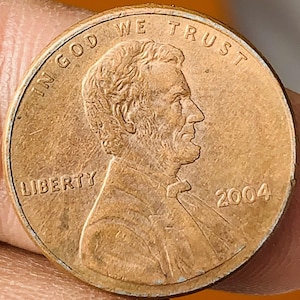 May include: A copper-colored United States penny coin from 2004. The obverse features a profile of Abraham Lincoln, with the inscriptions "IN GOD WE TRUST" and "LIBERTY".