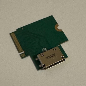 Peut inclure: Une carte de circuit imprimé verte avec un connecteur doré portant la mention "5225". La carte est de forme rectangulaire avec un bord cranté et une petite découpe circulaire. Le connecteur est argenté.