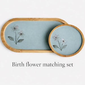 May include: A matching set of a light blue tray and coaster with a floral design. The tray is oval-shaped with a wooden frame, and the coaster is round. The text "Birth flower matching set" is below the items.
