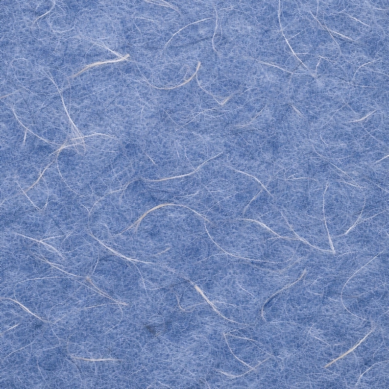 May include: Close-up of textured, light blue paper with white, thread-like fibres scattered across the surface. The paper has a soft, fibrous appearance, with the white fibres creating a delicate, organic pattern.