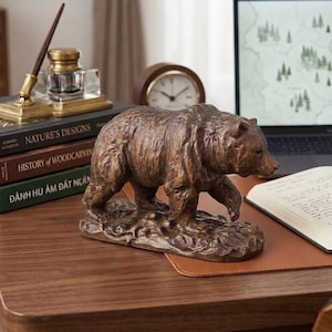 May include: A detailed brown bear sculpture, crafted with textured details, stands on a small base. The bear is positioned on a wooden desk, near books, a clock, and a laptop. The sculpture adds a rustic touch to the workspace.