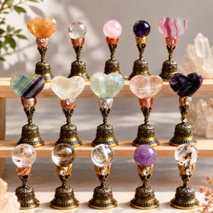 May include: A collection of fifteen decorative wax seal stamps arranged on a wooden shelf. Each stamp features a unique polished gemstone topper in heart or sphere shapes, mounted on an ornate, antique-style brass handle with metal leaf details.