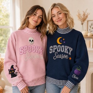 May include: Two long-sleeve sweatshirts with mock necks and gingham trim. The pink sweatshirt features a skull, the text "SPOOKY Season," and a black cat. The navy sweatshirt features a moon, stars, the text "SPOOKY Season," and a purple cauldron.
