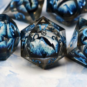 Puede incluir: Juego de dados poliédricos con cuerpo de resina transparente y detalles azules. Los dados presentan un patrón azul y blanco arremolinado en el interior, con números azules. Los dados están diseñados para juegos de mesa.