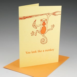 May include: A yellow card with a red monkey holding a banana and hanging from a branch. The text "You look like a monkey" is printed on the card.