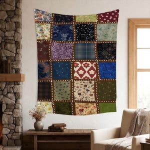 Peut inclure: Une grande tenture murale en patchwork avec une variété de carrés de tissu à motifs floraux dans les tons de bleu, vert, rouge et marron. Les carrés sont bordés d'un tissu marron foncé et de lignes pointillées blanches. La tapisserie est suspendue au-dessus d'une table en bois.