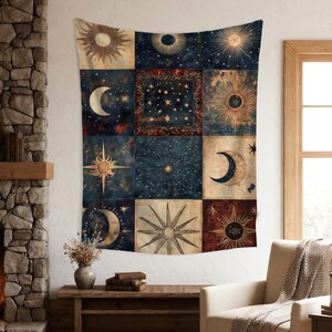 May include: A large tapestry with a celestial design featuring suns, moons, and stars in a patchwork pattern. The colour scheme includes navy blue, beige, and burgundy, creating a vintage aesthetic. The tapestry is displayed on a white wall.