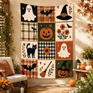 Op de afbeelding: Een rechthoekig wandkleed met een raster van negen vierkanten met Halloween-motieven, waaronder geesten, pompoenen, zwarte katten, vleermuizen, een heksenhoed, een bezem en bloemen, tegen een achtergrond van ruit- en blokpatronen.