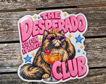 May include: A die-cut sticker featuring a fluffy brown cat wearing a gold crown and pink sunglasses. The cat sits beside a cocktail glass with a cherry. The text reads THE DESPERADO CLUB and SO FUN IT HURTS, surrounded by small blue and yellow stars.