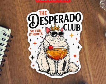 May include: A die-cut sticker featuring a fluffy white cat wearing a gold crown and black sunglasses. The cat holds a cocktail glass with a cherry. Text reads THE DESPERADO CLUB SO FUN IT HURTS, surrounded by small orange and black star icons.
