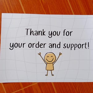 Op de afbeelding: Een rechthoekige witte kaart met een lichtgrijs ruitpatroon. De tekst luidt, Thank you for your order and support! Onder de tekst staat een eenvoudige lijntekening van een beige stokfiguurtje met opgeheven armen en een lachend gezicht.