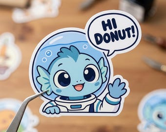 May include: A die-cut sticker featuring a light blue aquatic creature wearing a white astronaut helmet. The character is waving and has a speech bubble with the text HI DONUT! in dark blue letters. The design uses shades of blue and white.