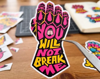 May include: A die-cut sticker shaped like a gauntlet featuring the text YOU WILL NOT BREAK ME in bold pink and yellow lettering. The design includes a small graphic of white boxer shorts with red hearts in the center of the text.